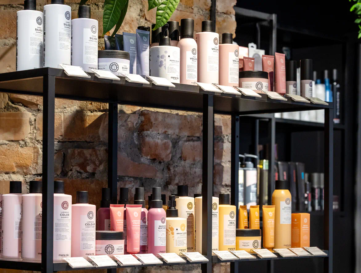 Hyllor med professionella hårvårdsprodukter i salongen mot en rustik tegelvägg.