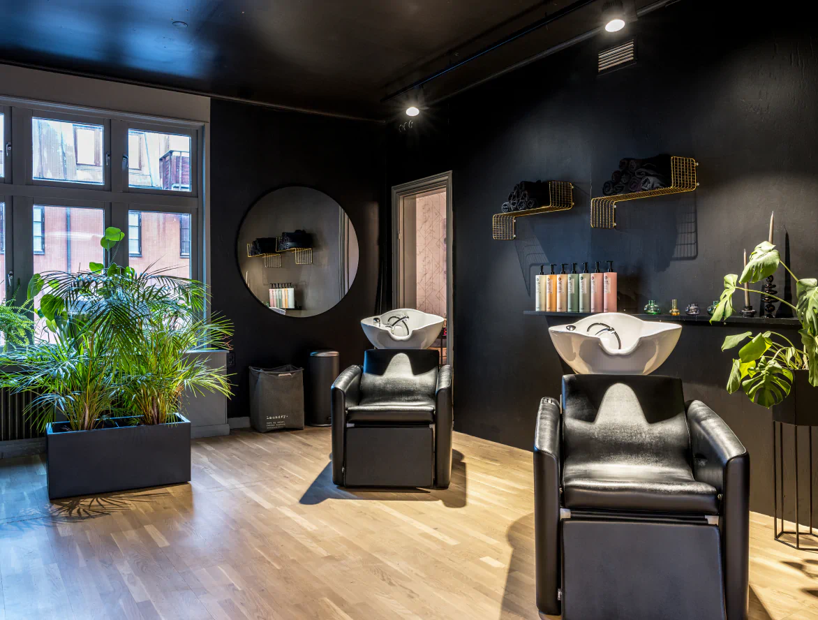 Tvättstationer i en modern frisörsalong med svarta väggar, gröna växter och stora fönster.